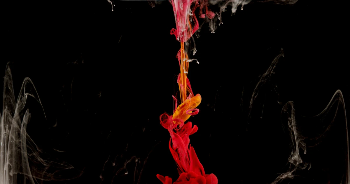 A plume of red and gold ink falling through dark water, pale threads of white drifting on either side of it